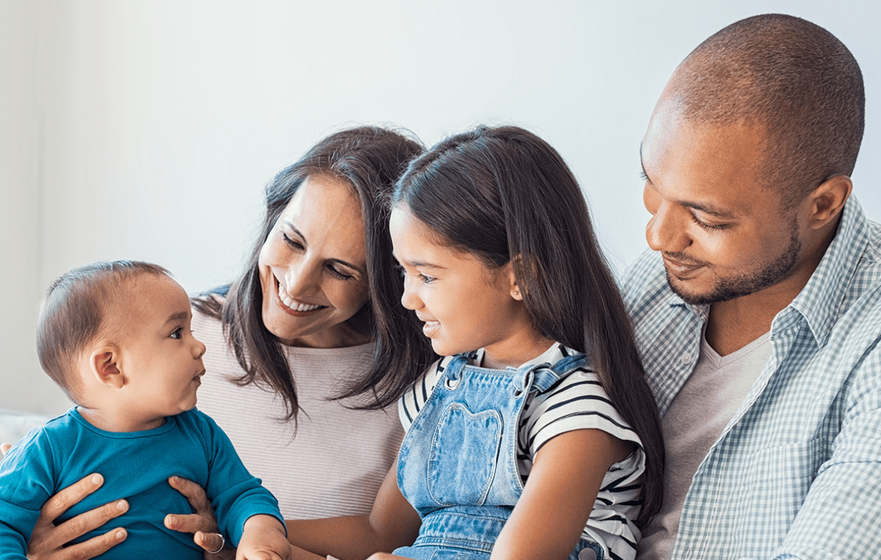 Photograph of family of four sitting together and looking at each other contentedly. 