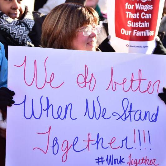 Woman holding sign that says "We do better when we stand together"